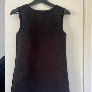 Svart kort klänning med rosett  - Snygg svart ärmlös kort klänning från Divided by H&M storlek xs . Klänningen har en djup v-ringning baktill med en söt rosettdetalj. Enkel och stilren design i slätt material, perfekt för dig som gillar minimalistisk look. Endast använd 1 gång, inga defekter! 100kr💕