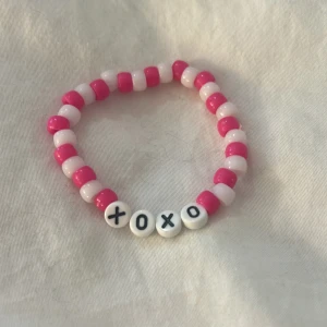 XOXO armband - Supergulligt armband med rosa och vita pärlor. Armbandet har fyra vita bokstavspärlor med texten 'XOXO' i svart. Perfekt accessoar för att ge din outfit lite extra kärlek och färg. OBS, katt finns i hemmet! Armbandet är gjort av mig!