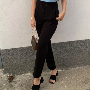 Svarta kostymbyxor med bälte - Snygga svarta kostymbyxor med hög midja och tillhörande bälte. Byxorna har raka ben och stilrena pressveck framtill som ger en clean look. 