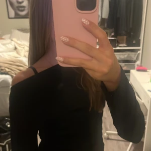 Svart offshoulder topp med scrunchad på sidor - Säljer en svart långärmad lite tjockare topp med offshoulder-design och scrunch. Sitter tight och har en stilren look som passar perfekt till jeans eller kjol. Tunt men varmt och stretchigt material som känns skönt mot huden. Enkel men ändå trendig modell.