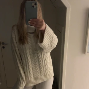 Vit stickad polotröja med kabelmönster - Mysig vit stickad polotröja med grovt kabelstickat mönster och breda ärmar. Tröjan har en hög polograge som kan vikas. Världens mysigare höst tröja. I väldigt bra skick därav att den är helt ny och endast är testad aldrig använd.