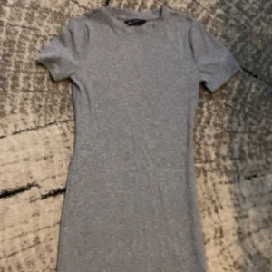 Grå ribbad kortklänning LCW Vision - Säljer en enkel och stilren grå ribbad kortklänning från LCW Vision i storlek S. Klänningen har korta ärmar och rund hals, med en slim passform som sitter snyggt på kroppen. Perfekt för dig som gillar minimalistisk och bekväm stil.