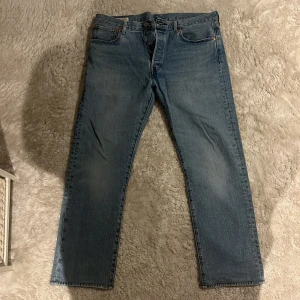 Levi's 501 ljusblå jeans W34 L32 - Klassiska Levi's 501 jeans i ljusblå tvätt med raka ben och knappgylf. Jeansen har fem fickor, ikonisk läderpatch bak och röd Levi's-tagg på bakfickan. Tillverkade i slitstarkt bomullsjeans, perfekt för en avslappnad och tidlös look.