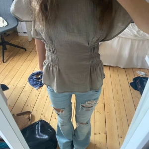 Grön blus med rynkade detaljer - Säljer en grön  blus med korta, vida ärmar och snygga rynkade partier i midjan som ger en markerad siluett. Blusen har en lätt struktur i tyget och faller fint över kroppen. Perfekt för dig som gillar en avslappnad men ändå trendig look.