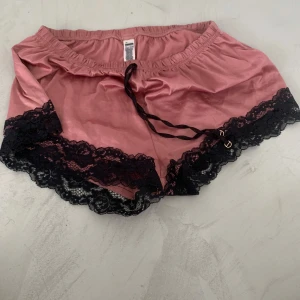 Rosa satinshorts med svart spets - Snygga rosa shorts i satin med svart spetskant och snörning i midjan. De har en loose passform och känns riktigt mjuka och lyxiga. Perfekta för sommarkvällar eller när du vill chilla hemma med stil.