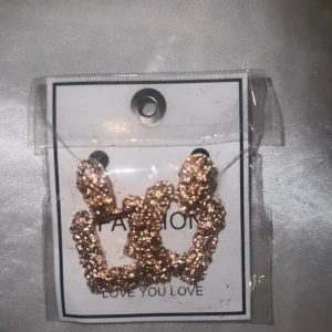 Glittriga guldörhängen i unik form - Säljer ett par coola örhängen i guld med glittrig yta. De har en unik, lite kantig form som verkligen sticker ut och passar dig som gillar att synas. Perfekta för att ge din outfit extra edge och glam.