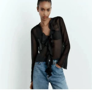 Svart transparent blus med volang - Svart transparent blus med långa ärmar och djup v-ringning. Blusen har volangkant längs ringningen och knyt framtill. Perfekt till fest!                     Använd fåtal gånger 😊