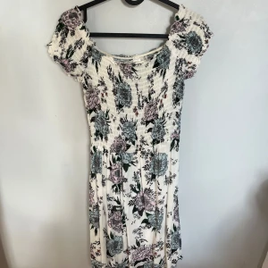 Blommig kortklänning med smock H&M - Supersöt kortklänning med smockad överdel och offshoulder-ärmar från hm. Klänningen är vit med blommigt mönster i pastelliga toner av blått och rosa. Den har en luftig kjol och materialet känns mjukt och stretchigt. Använd fåtal gånger men har inga tecken på användning och inga defekter.