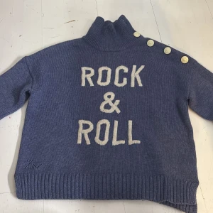 Blå stickad polotröja Zadig & Voltaire - Blå stickad polotröja från Zadig & Voltaire med texten 'ROCK & ROLL' i vitt framtill. Tröjan har hög krage, dekorativa knappar på axeln. Använts mycket förut men är välldigt skön och mysig. Dock lite osäker i storlek S-xs
