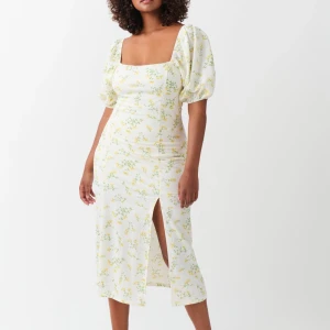 Blommig långklänning från Gina Tricot - Superfin midiklänning från Gina Tricot i vitt med gult och grönt blommönster. Klänningen har puffiga korta ärmar, fyrkantig ringning och en snygg slits framtill. Perfekt för sommarens alla tillfällen! Storlek XL, normal i storlek. Finns lite elastan. Använd en gång, som ny!