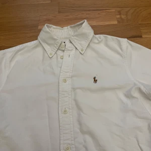 Vit skjorta från Polo Ralph Lauren XS - Klassisk vit skjorta från Polo Ralph Lauren i bomull, custom fit. Skjortan har lång ärm, knappar hela vägen och ikoniska broderade loggan på bröstet. Perfekt krage och stilren look som funkar till allt.