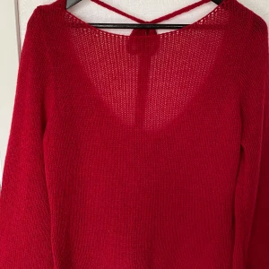 Röd stickad tröja med knyt från SHEIN - Snygg röd stickad tröja från SHEIN i storlek M. Tröjan har djup urringning både fram och bak samt en fin knytning i ryggen. Långärmad och i ett lätt, luftigt material av polyester. Perfekt för dig som gillar en enkel men ändå unik look.