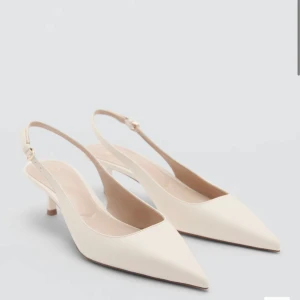 Beige pumps med spetsig tå och låg klack - Stilrena pumps i beige med spetsig tå och smal låg klack. Skorna har öppen häl med justerbart spänne. Skit snygga och så så populära. Helt slutsålda och svåra att få tag på. Perfekta inför en utekväll, middag eller till kontoret😍