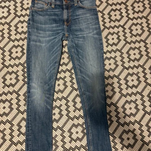 Blå jeans från Nudie Jeans Co W30 L32 - Snygga blå jeans från Nudie Jeans Co med klassisk femficksdesign och coola orangea sömmar på bakfickorna. Modellen har en slim passform och raka ben, tillverkade i slitstarkt jeanstyg. Perfekt för dig som gillar stilrena och tidlösa jeans.