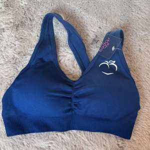 Mörkblå sporttopp Peach Athletics S - Sportig mörkblå topp från Peach Athletics med brottarrygg och diskret rynk framtill. Stilren logga i vitt på bröstet och bred resår nedtill för extra stöd. Perfekt för dig som vill ha en bekväm och snygg topp till träningen.