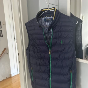 Mörkblå dunväst från Polo Ralph Lauren - Snygg mörkblå dunväst från Polo Ralph Lauren med gröna dragkedjor och en unik insida! Storleken är XS, men passar  också S väldigt bra! Kontakta gärna vid frågor eller behov av fler bilder! Priset kan självklart diskuteras!🤝🏻💫