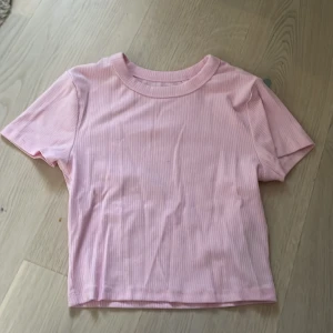 Ljusrosa ribbad t-shirt FSBN Sister - Supersöt ljusrosa t-shirt från FSBN Sister i ribbad bomull. Modellen är kortärmad med klassisk rund halsringning och har en enkel, clean look. Perfekt för dig som gillar en basic men ändå trendig vibe.