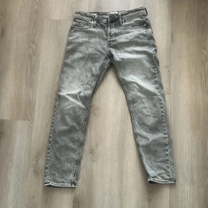 Grå jeans från Jack & Jones - Snygga grå jeans från Jack & Jones i modellen Tapered/Mike. Jeansen har klassisk femficksdesign, normalhög midja och avsmalnande ben. Tillverkade i slitstarkt denim med en tvättad look som ger en cool vibe. Storlek W30 L32.