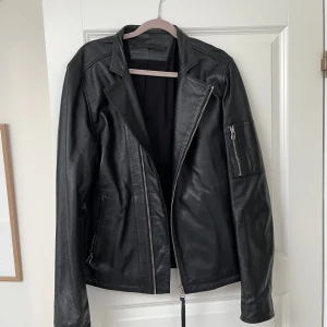 Svart skinnjacka från Tiger of Sweden - Snygg svart skinnjacka från Tiger of Sweden, modell RIKKI. Jackan har asymmetrisk dragkedja, klassisk krage och dragkedjor på fickor och ärm. Perfekt för dig som vill ha en stilren och tidlös look med edge. Använda 2-3 gånger. Nypris 3499. 