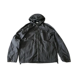 Svart Goggle Jacket från C.P. Company - Säljer en svart Goggle Jacket från C.P. Company med ikoniska glasögon i huvan. Jackan har dragkedja framtill, bröstficka med lock och justerbara ärmslut. Perfekt för dig som vill sticka ut. Ny pris ligger ungefär på 4000-5000kr. Mitt pris är 1999. Ställ gärna frågar! Kom privat om ni vill ha bilder på authenticity.