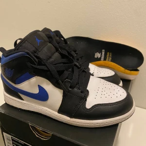 Nike Air Jordan 1 Mid Racer Blue - Nike Air Jordan 1 Mid i färgen Racer Blue med svart, vit och blå färgblock. Klassisk siluett med snörning, rund tå och perforerad tåbox. Skorna är i skinn och har den ikoniska Swoosh-loggan i blått på sidorna samt Jordan Wings-logga vid ankeln. Kunde tyvärr inte hitta de originala sulorna men man får Artapidrriska suler till skorna. Pris kan diskuteras 