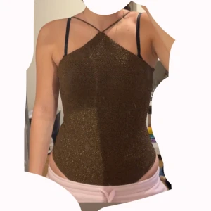 Glittrig brun body H&M - glittrig brun body från H&M med smala axelband som korsas framtill. Toppen är tight och har en snygg halterneck-liknande form, perfekt för att sticka ut. Materialet är stretchigt och skimrar i ljuset. Jätte fin för en night out. Storlek S, passar M oxå. Aldrig använd.