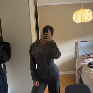Mörkgrå hoodie med dragkedja och matchande byxa - Säljer en mörkgrå hoodie med dragkedja och huva. Tröjan har långa ärmar och en avslappnad passform, perfekt för chill dagar. Materialet känns mjukt och skönt mot huden. Enkel och stilren design som funkar till det mesta.