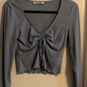 Blå croppad topp från NA-KD - Supersnygg blå croppad topp från NA-KD med v-ringning och långa ärmar. Toppen har ribbat tyg och en snygg snörning framtill som ger en cool detalj. Perfekt att styla med höga jeans eller kjol för en trendig look.