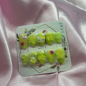 NeonPuff(S);Short Almond - Ett set med gelé press-on naglar i limegrönt med coola 3D-rosetter, hjärtan och söta kattmotiv. Naglarna har en glansig finish och mix av dekorationer i rosa, silver och gult. Formen är short almond och de kommer i storlek S: 15 mm, 11,5 mm, 12 mm, 11 mm, 9 mm. Perfekt för dig som vill sticka ut med färgglada och unika naglar.