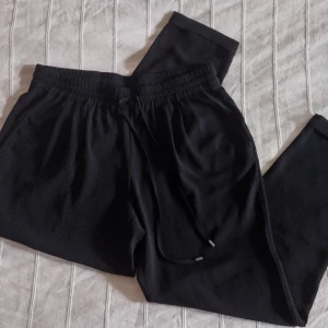 Zara svarta tunna byxor med resår - Svarta byxor med elastisk midja och snörning framtill. Byxorna är tunna och luftiga och har sidofickor och en passpoalficka med knapp i bak. De har bara använts ett par gånger och är i fint skick bortsett från att det finns tre små hål på benen i fram. 