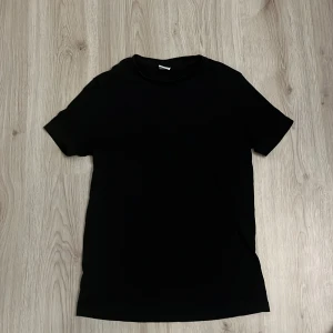 Svart t-shirt från Bershka - En klassisk svart t-shirt från Bershka i enkel och stilren design. T-shirten har rund halsringning och korta ärmar, perfekt för en clean och avslappnad look. Materialet känns mjukt och bekvämt mot huden.