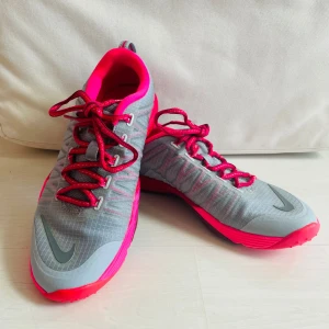 Nike sneakers strl 38 - Nike sneakers i grått med neonrosa detaljer och snörning. Snygg sportig design med reflekterande logga på sidan och tå. I princip oanvända, mycket fint skick!
