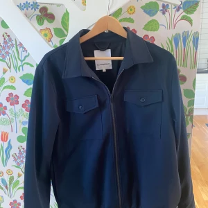 Mörkblå overshirt från Lindbergh - Snygg mörkblå overshirt från Lindbergh med klassisk krage, två bröstfickor med lock och knappar samt dragkedja framtill. Perfekt lager-på-lager-plagg med stilren look och raka linjer. Passar dig som gillar enkel och clean stil. Nypris från Boozt 1299, hör av er vid eventuella frågor eller fler bilder!