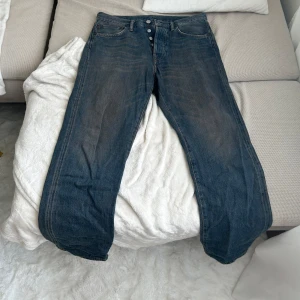 Acne Studios blå jeans 30/30 - Snygga blå jeans från Acne Studios i klassisk rak modell. Jeansen har knäppning fram, fem fickor och coolt läderpatch bak i midjan. Tillverkade i 100% bomull för en autentisk jeanskänsla. Perfekta till sneakers eller boots.