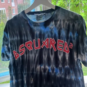 Tie-dye t-shirt från Dsquared2 - Snygg tie-dye t-shirt från Dsquared2 i svart, blått och vitt med stort rött Dsquared2-tryck på bröstet. Klassisk rund hals och korta ärmar. Perfekt för dig som vill sticka ut med en cool streetstyle-look.