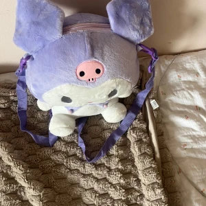 Lila Kuromi ryggsäck i plysch - Supergullig ryggsäck formad som Kuromi från Sanrio, i mjuk plysch. Väskan är lila och vit med rosa detaljer och har justerbara axelband samt dragkedja upptill. Perfekt för dig som älskar kawaii och vill sticka ut med en unik accessoar.