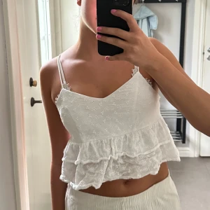 Vit broderad linnetopp med volang - Superfin vit linnetopp med tunna axelband och broderade små blommor. Toppen är croppad och har dubbla volanglager nedtill. Vet inte var den är ifrån då lappen är bortklippt.