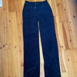 Svarta mjukisbyxor Juicy Couture XXS - Svarta mjukisbyxor från Juicy Couture i supermjuk velour med bred resår och snörning i midjan. Byxorna har raka ben, stora fickor fram och bak med knappdetaljer. Perfekta för en chill och trendig look. Nästan aldrig använda