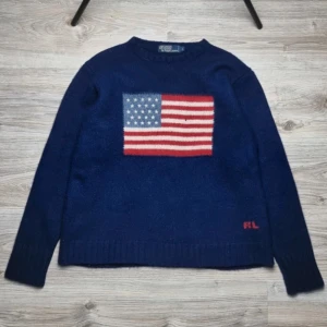 USA Ralph Lauren tröja - Sällsynt Ralph Lauren tröja i marinblå ull med amerikanska flaggan på bröstet🇺🇸🤩  Storlek: L (sitter som M) Nypris: 5000 kr – extremt svår att få tag på!  Skick: Mycket bra, endast ett litet hål (se bild 2) Mått: – Bröst: 54 cm – Längd: 61 cm  Pris kan sänkas endel vid snabb affär!🙌 Hör av av dig vid minsta fundering!👏