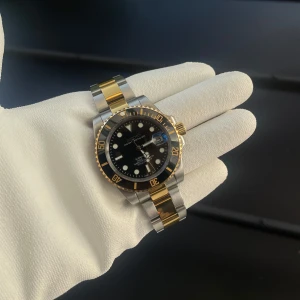 Seiko ”two-tone” submariner - Snygg Seiko mod klocka med svart urtavla och datumvisning. Den har en tvåfärgad länkarmband i silver och guld samt en svart vridbar bezel med guldfärgade markeringar. Perfekt för den som vill ha en stilren och elegant look.