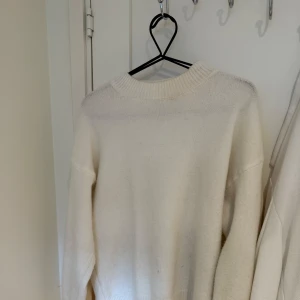 Vit stickad tröja - En vit stickad tröja med rund halsringning och långa ärmar. Tröjan har ribbade muddar vid hals, ärmslut och nederkant. Passar både på kille och tjej