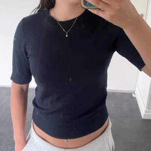 Mörkblå stickad kortärmad tröja - En basic mörkblå stickad tröja från lager 157 med korta ärmar och rund halsringning. Tröjan har ribbade muddar vid ärmslut och nederkant, vilket ger en clean och stilren look. Perfekt att matcha med jeans eller kjol för en chill vibe.