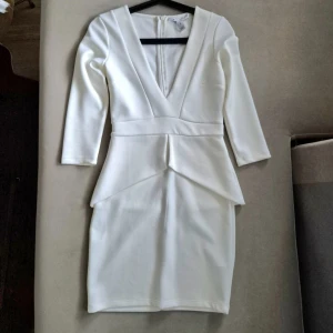 Vit kort klänning med v-ringning - Snygg vit kort klänning från NLY One med djup v-ringning och trekvartsärm. Klänningen har markerad midja och coola detaljer vid höfterna som ger en modern siluett. Perfekt för dig som vill sticka ut med stilren look.