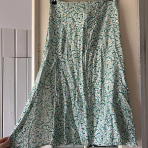 Blommig långkjol från SHEIN - Superfin långkjol från SHEIN med grönt och vitt blommönster och små gula detaljer. Kjolen har en smickrande A-linjeform och dragkedja bak. Perfekt för dig som vill ha en somrig och färgglad look.