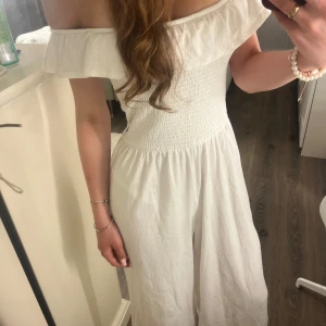 Vit byxdress med volangkrage - Superfin vit byxdress från Ü i storlek 152. Off shoulder-modell med volangkrage och smockad överdel. Vida ben och mjukt, lätt bomullstyg som känns luftigt och skönt.