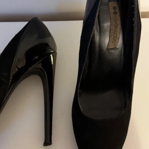 Svarta pumps med hög klack Even&Odd - Snygga svarta pumps från Even&Odd med hög klack och plattform. Skorna har en blandning av matt och glansig finish, spetsig tå och klassisk siluett. Perfekta för dig som vill ha en stilren och elegant look.