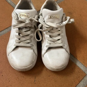 Vita sneakers från Polo Ralph Lauren - Klassiska vita sneakers från Polo Ralph Lauren i 100% skinn med snygga detaljer och logga på sidan och plösen. Skorna har rund tå, platt sula och snörning. Perfekta för en clean och stilren look.