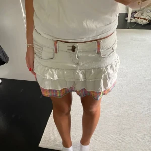 Vit volangkjol med färgglada detaljer - Supersöt vit kortkjol med volanger och färgglad rutkant längst ner. Kjolen har jeanslook, bälteshällor med färgade detaljer och fickor fram. Perfekt för dig som behöver en ny kjol till sommaren!!🥳🥰☀️Kjolen passar mig som vanligtvis har S, skriv förslag på pris!!!!