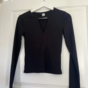 Svart ribbad långärmad topp - Svart långärmad topp med ribbad struktur och snygg v-ringning framtill. Tight passform som framhäver siluetten och passar perfekt till jeans eller kjol. Enkel men trendig design som funkar året runt.