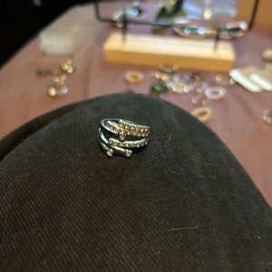 Silverfärgad ring med glittriga stenar - Cool statementring i silverfärg med flera lager som slingrar sig runt fingret. Ringen är dekorerad med glittrande stenar på varje band, vilket ger en riktigt lyxig och trendig look. Perfekt för dig som vill sticka ut och addera lite extra bling till din outfit.